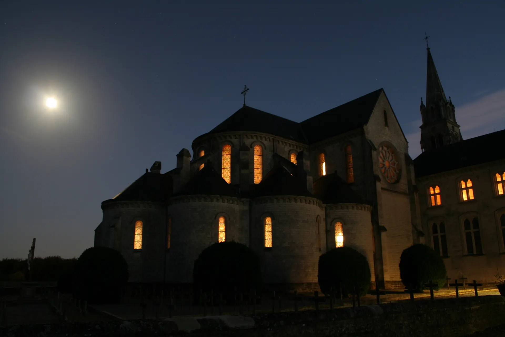 L’église abbatiale la nuit, ses vitraux éclairés de l’intérieur, sous la pleine lune