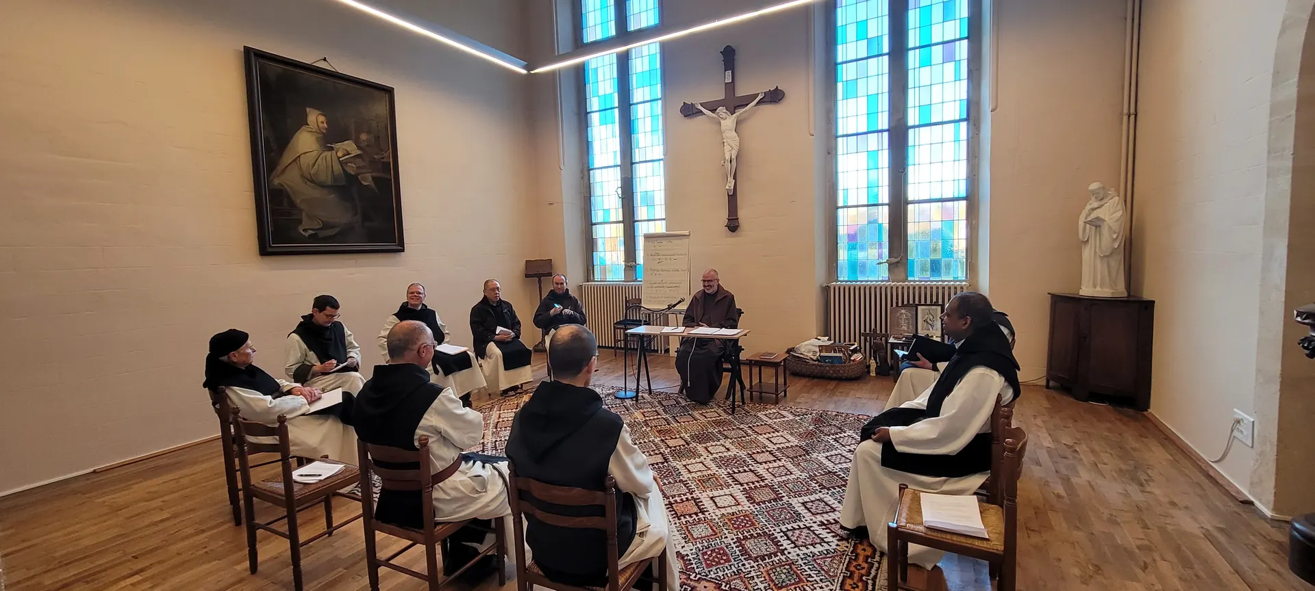 Les frères réunis en cercle autour du père abbé, sous le crucifix et les vitraux