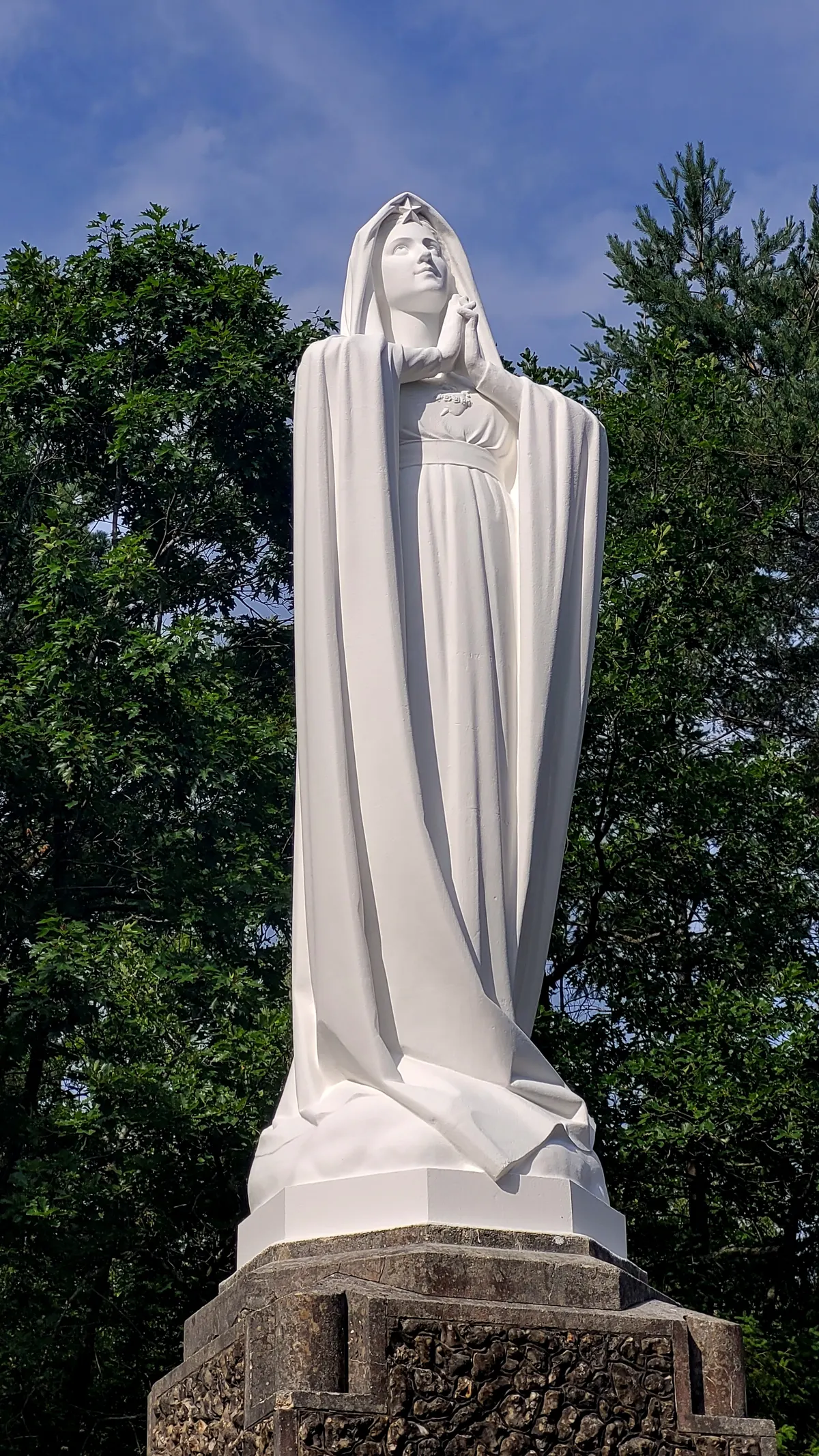 La statue blanche de Notre-Dame de la Confiance, en pied, devant les arbres