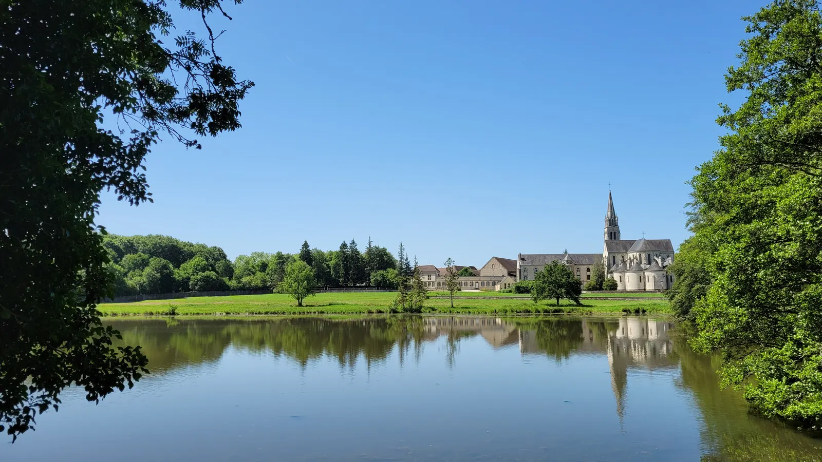 L’abbaye et son clocher vus de l’autre rive de l’étang, sous un ciel bleu de juin