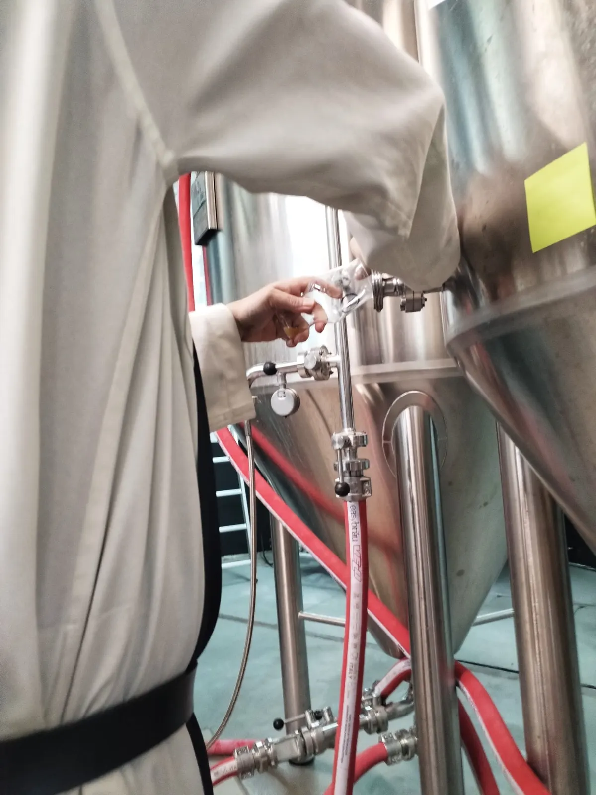 Une main ouvre le robinet d’une cuve de brassage en inox