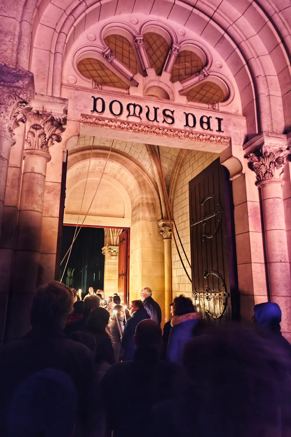 Les fidèles, cierges en main, passent la porte de l’église sous l’inscription Domus Dei, de nuit